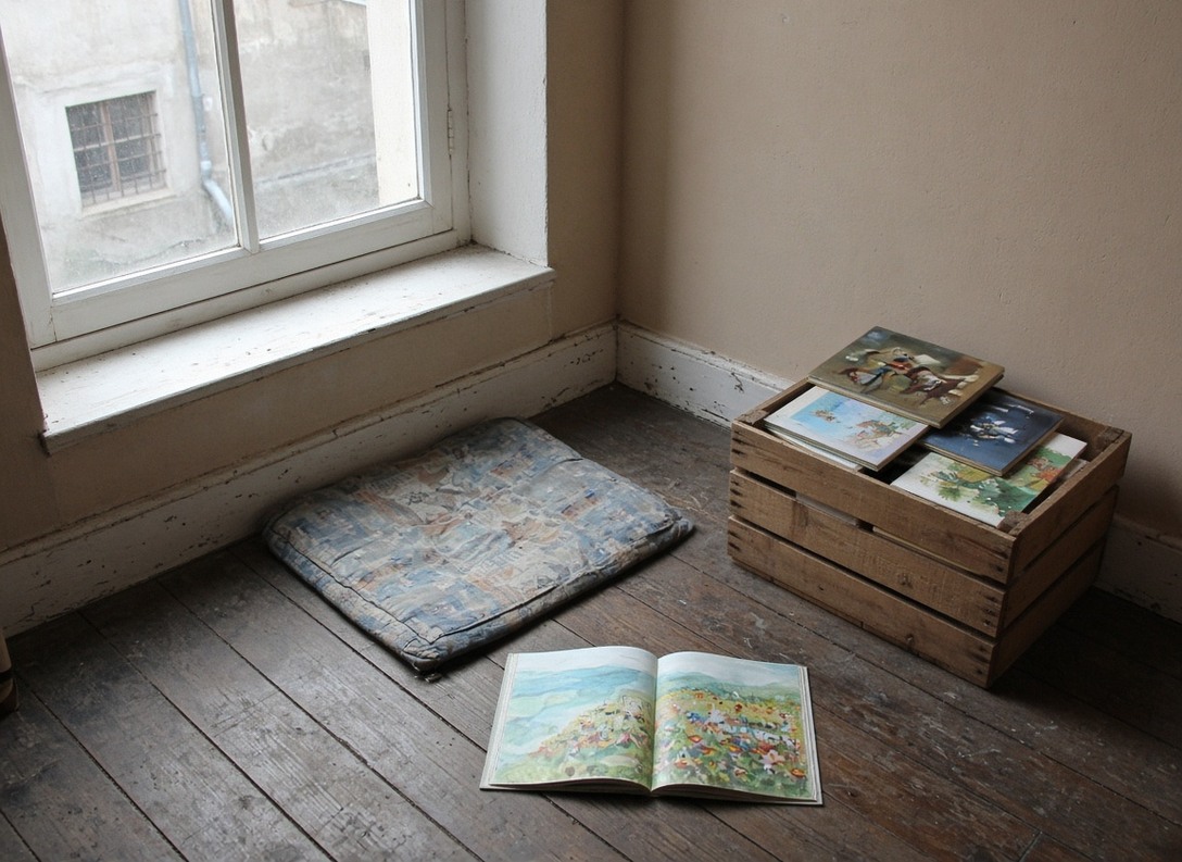 Bodensitzkissen, aufgeschlagenes Bilderbuch und Holzkiste mit Kinderbüchern